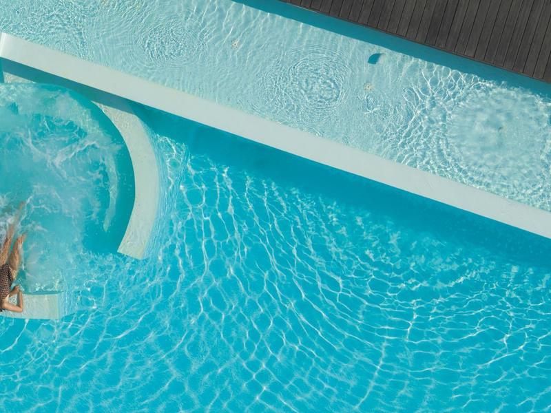 Person entspannt sich am Rand eines sauberen, blauen Hotelpools auf einer Terrasse.