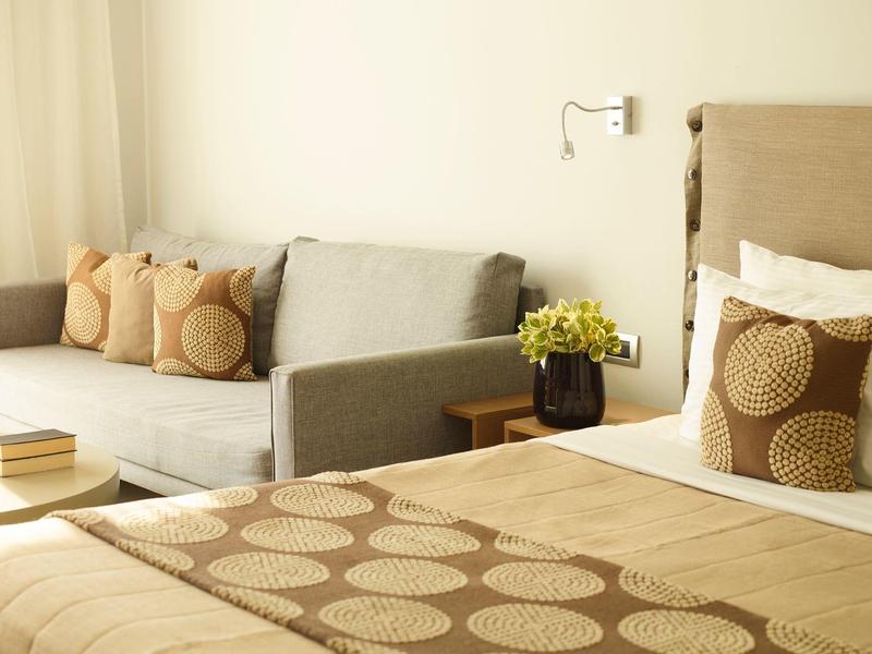 Gemütliches Wohnzimmer mit grauem Sofa, kleinen Kissen und dekorativem Beigebett mit kreisförmigem Muster.