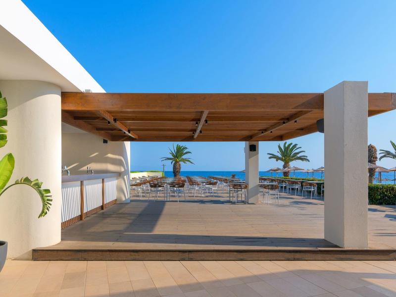 Moderner Außenbereich mit Pergola, Blick aufs Meer und Palmen im Hintergrund bei klarem Himmel