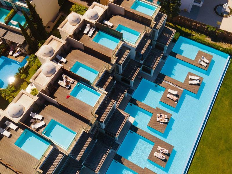 Luftaufnahme von modernen Hotelzimmern mit privaten Pools und Sonnendecks am Wasser.
