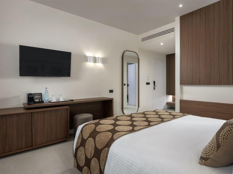 Modernes Hotelzimmer mit großem Bett, Fernseher an der Wand und Holzmöbeln.