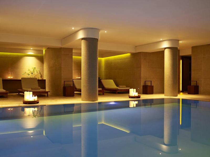 Ein moderner Innenpool mit bequemen Liegen und warmem Licht im Hintergrund.