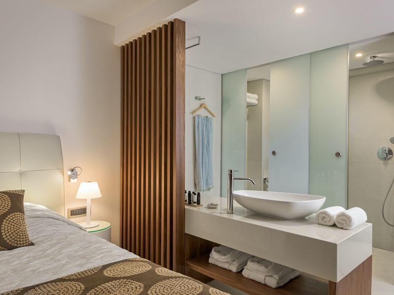 Modernes Hotelzimmer mit Bett und offenem Bad mit Waschbecken und Dusche.