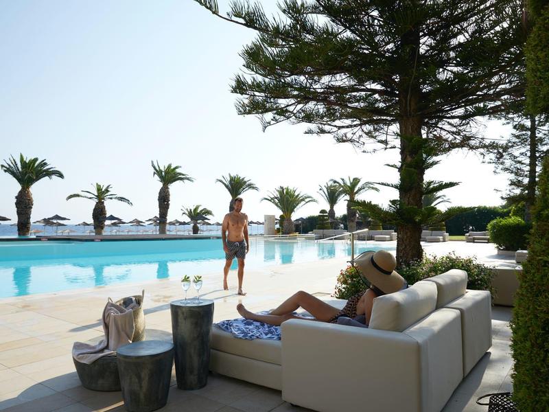 Frau entspannt auf Sofa neben Pool mit Blick auf Palmen und Meer.
