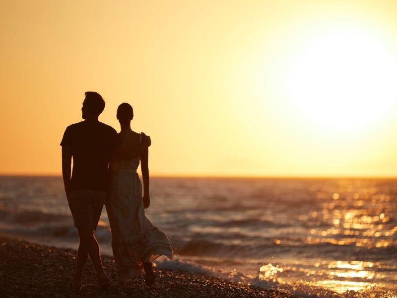 Zwei Personen gehen am Strand bei Sonnenuntergang spazieren.
