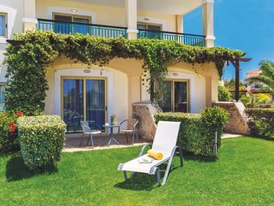 Ogród hotelowy z leżakiem na trawie i tarasem porośniętym roślinami pnącymi na budynku.