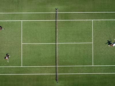 Widok z lotu ptaka na kort tenisowy z czterema zawodnikami grającymi w deblu.