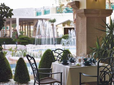 Tavolo elegantemente apparecchiato accanto a una fontana in un giardino d'hotel con piante verdi.