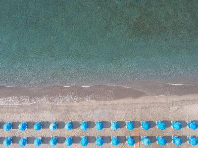 Widok z powietrza na plażę z rzędami niebieskich parasoli na piaszczystym brzegu.