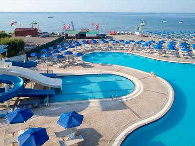 Grande piscina all'aperto con scivolo d'acqua, ombrelloni blu e vista sul mare.