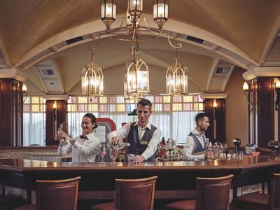 Tre bartender preparano cocktail al bancone di un elegante hotel.