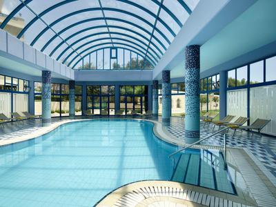 Grande piscina coperta con cupola di vetro, colonne e lettini ai lati.