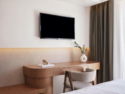 Moderner Hotelzimmer-Arbeitsbereich mit Fernseher, eleganter Holzkonsole und gemütlichem Stuhl.