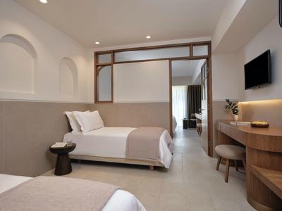 Modern eingerichtetes Hotelzimmer mit zwei Betten, Holzmöbeln und Flachbildfernseher an der Wand.