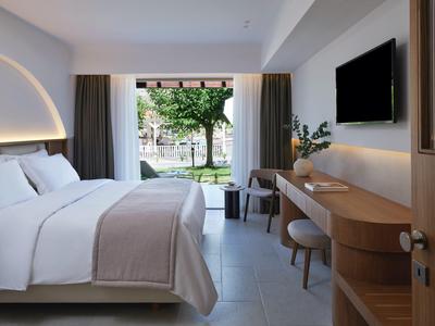 Modernes Hotelzimmer mit großem Bett, Schreibtisch, TV und Blick auf einen Garten.