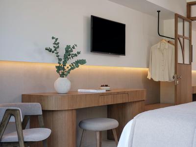 Modernes Hotelzimmer mit Schreibtisch, TV, Sitzgelegenheiten und Kleidungsständer.