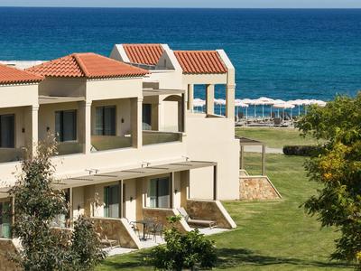 Modern hotel building by blue sea with garden and sun umbrellas.