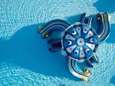 Colorful inflatable play structure with water slides in a clear pool.