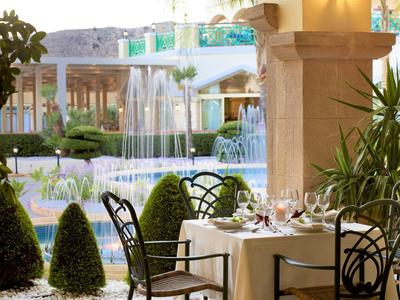 Elegant garden table with set glasses and chairs beside a fountain in a hotel setting.