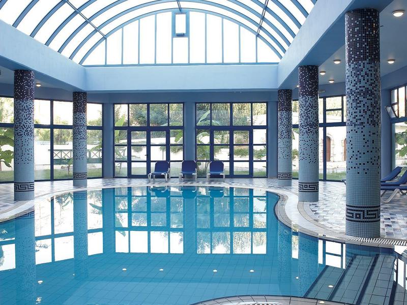 Piscina interna con tetto in vetro arcuato e colonne moderne in un hotel.