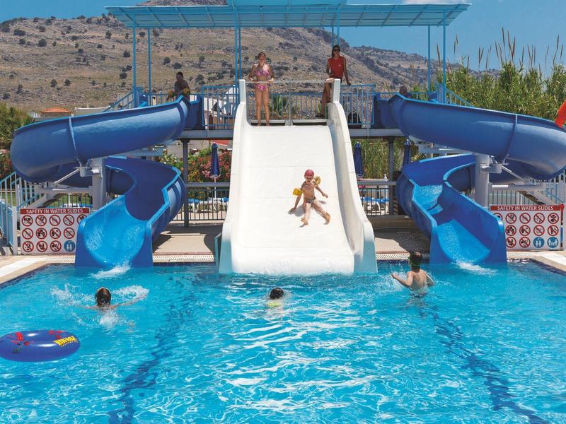 Parco acquatico con piscina, tre scivoli e bambini che giocano nell'acqua.