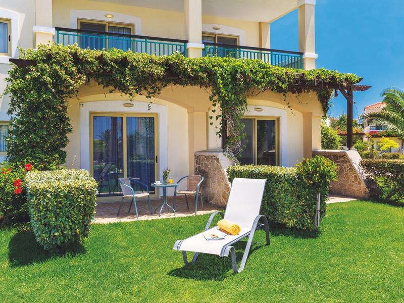 Giardino dell'hotel con cespugli verdi, sdraio sul prato e area pranzo esterna sotto pergolato.