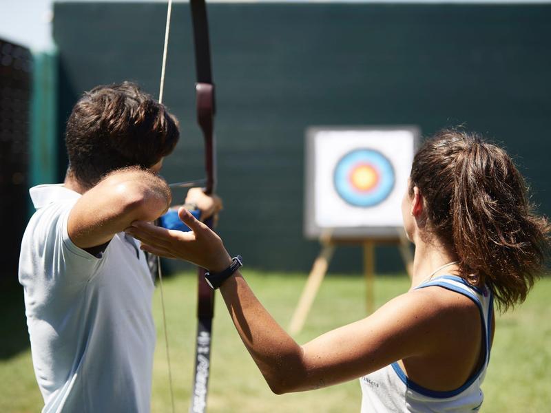 Due persone che praticano il tiro con l'arco con un bersaglio sullo sfondo in una giornata di sole.
