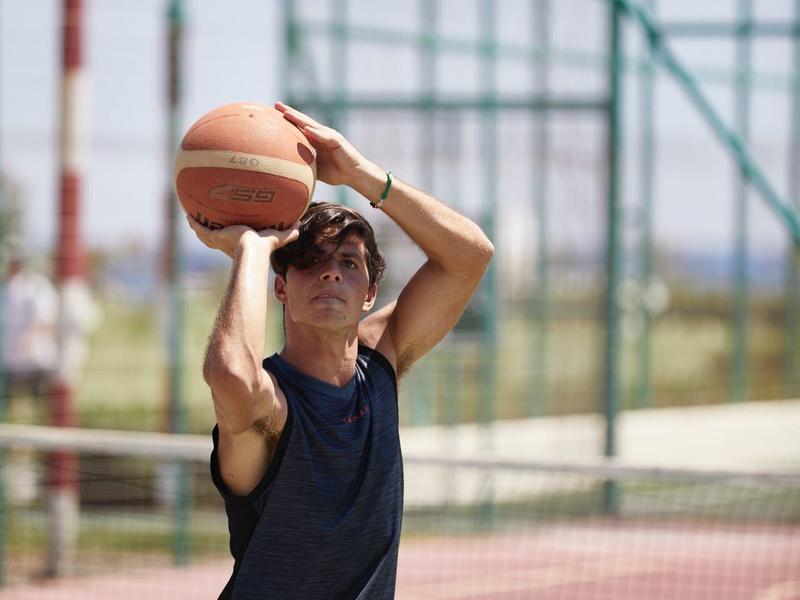 Persona gioca a basket su un campo all'aperto con tempo soleggiato.