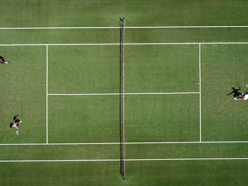 Vista aerea di un campo da tennis con tre giocatori su prato verde