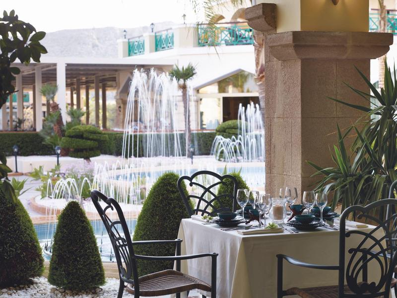 Tavolo elegantemente apparecchiato accanto a una fontana in un giardino d'hotel con piante verdi.