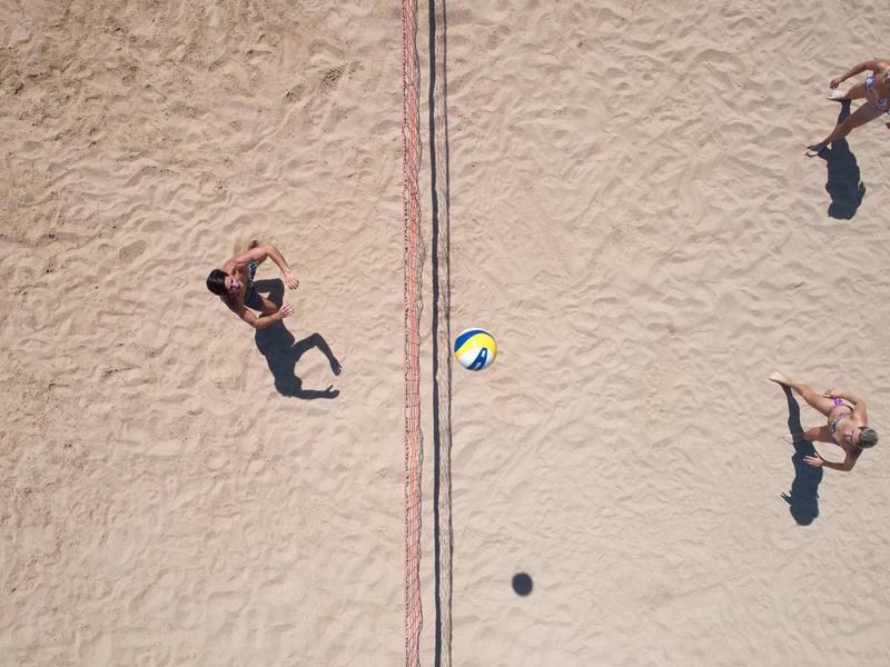 Tre persone giocano a beach volley su un campo sabbioso visto dall'alto.