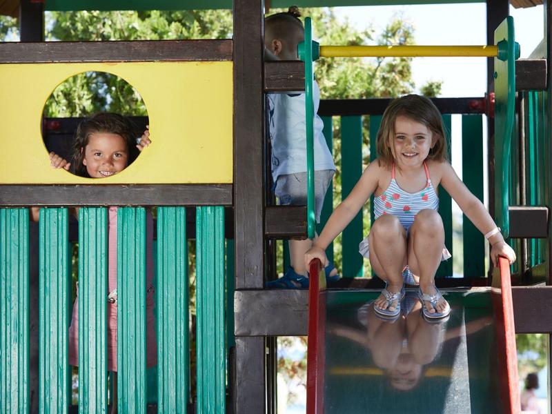 Bambini che giocano in un parco giochi colorato con scivolo all'aperto al sole.