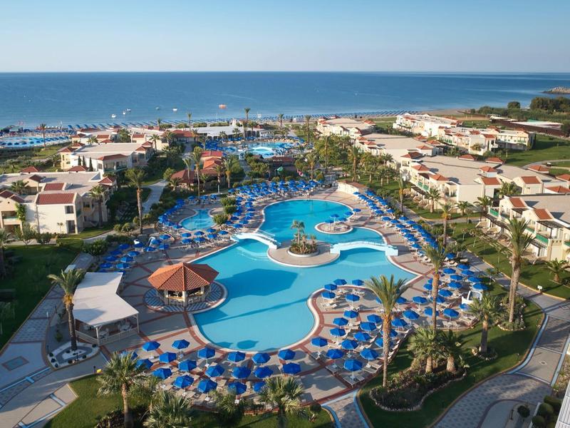 Grande piscina dell'hotel con ombrelloni e lettini, circondata da edifici vicino al mare.