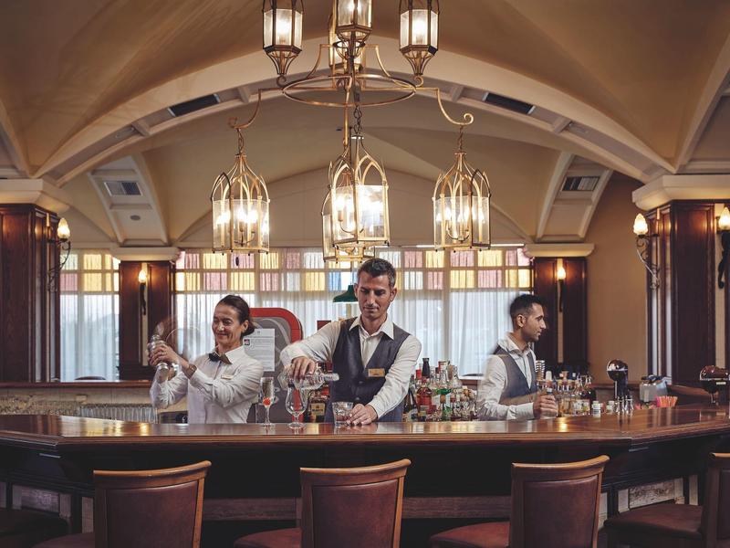 Tre bartender preparano cocktail al bancone di un elegante hotel.