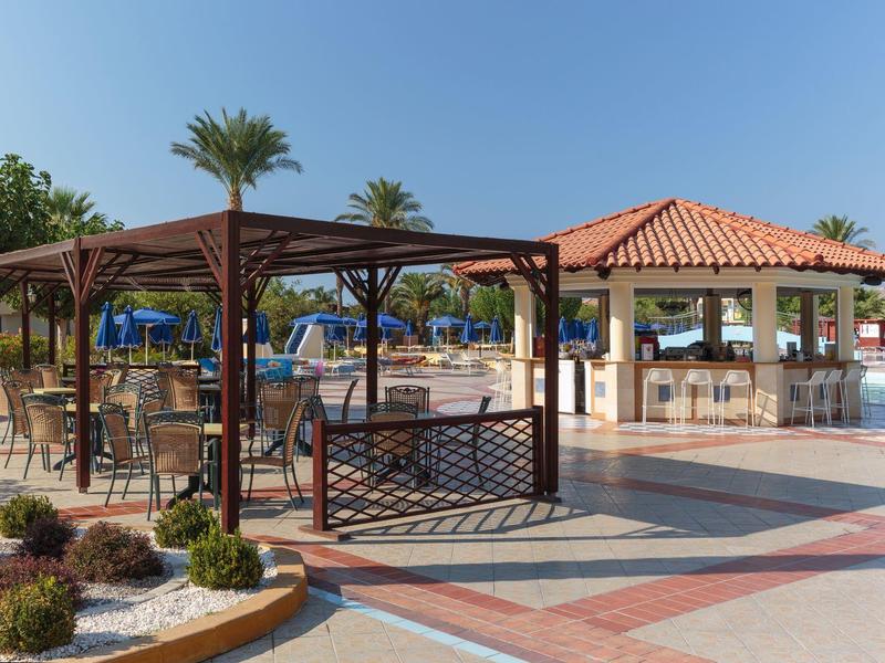 Area ricreativa con tavoli, sedie e bar a bordo piscina sotto il cielo azzurro in un resort