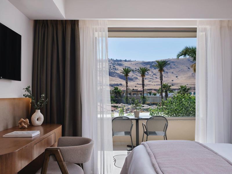 Camera d'hotel luminosa con balcone, vista sul mare e palme in lontananza.