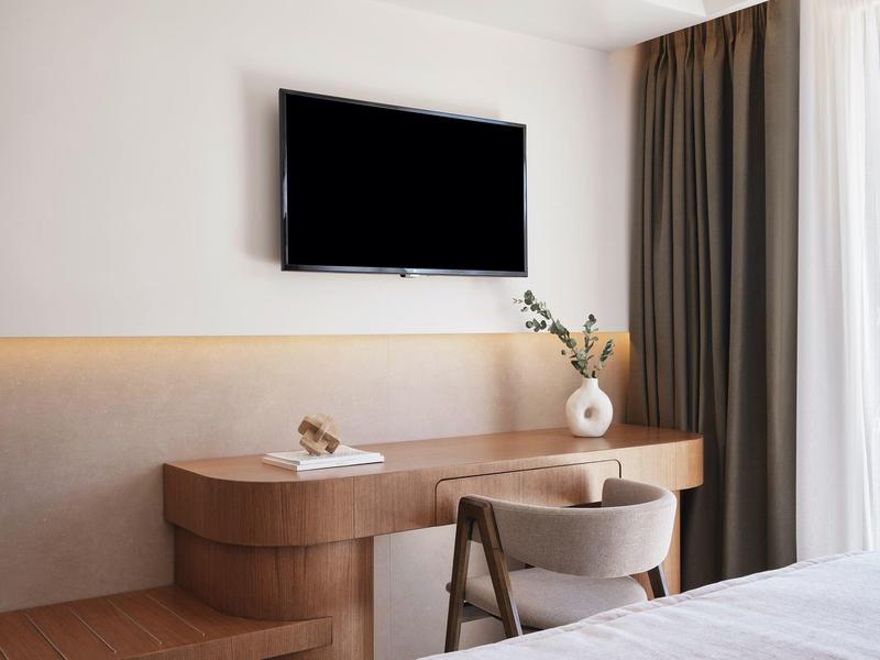 Spazio lavoro moderno con scrivania in legno, sedia, vaso e grande TV a muro.