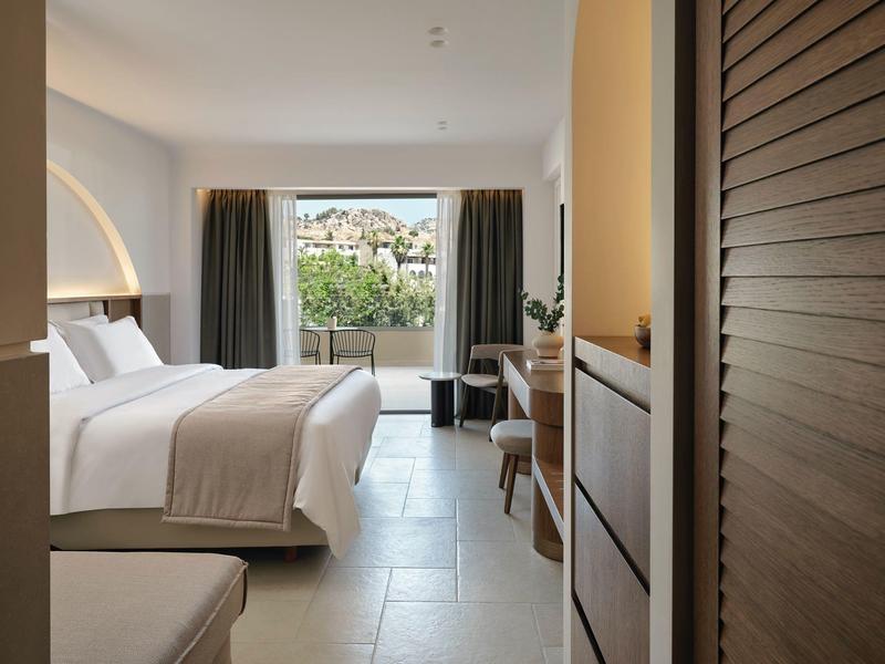 Camera d'hotel moderna con letto grande, terrazza e vista su colline verdi.