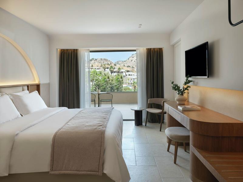 Camera d'hotel moderna con letto matrimoniale, scrivania, TV e balcone con vista sulla città