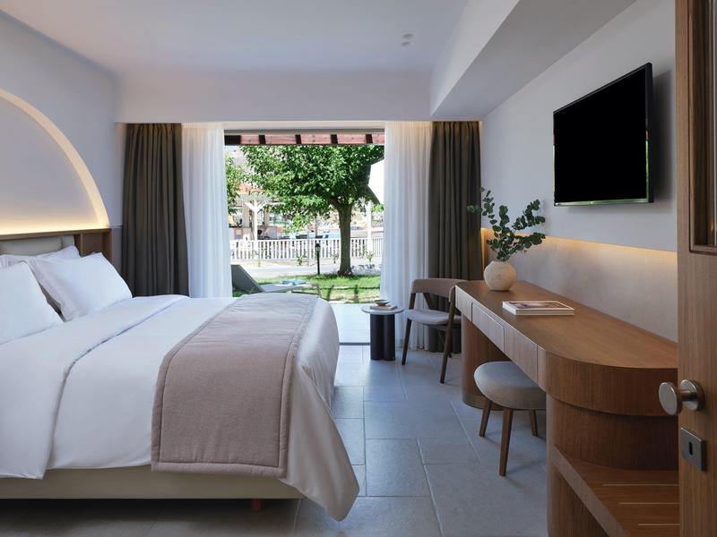 Camera d'hotel moderna con letto matrimoniale, scrivania, TV e vista sul giardino.