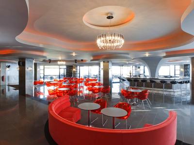 Lounge d'hotel moderno con divani rossi curvi, tavoli rotondi e lampadari.