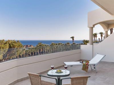 Balcone con tavolo, sedie e sedia a sdraio con vista su palme e oceano.