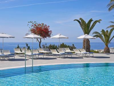 Outdoor-Pool mit Liegestühlen, Sonnenschirmen und Meerblick bei klarem Himmel.