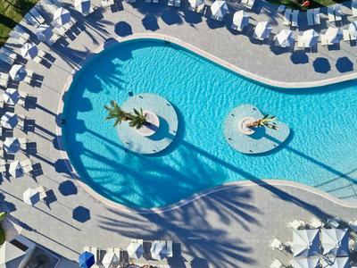 Poolbereich mit blauer Wasserfläche und Sonnenschirmen, Schatten von Palmen sichtbar