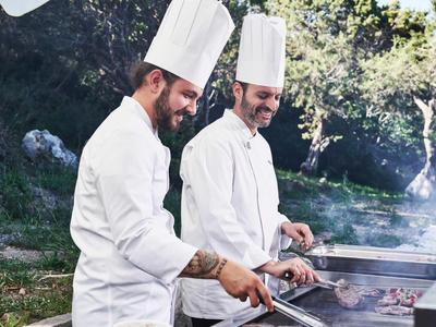 Zwei Köche in weißen Uniformen grillen im Freien auf einem Grill im Garten.