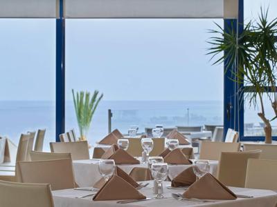 Sala da pranzo elegante con tavoli apparecchiati e vista sul mare tramite grandi finestre.