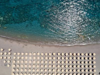 Vista aerea di una spiaggia con file di ombrelloni bianchi vicino ad acqua turchese limpida.