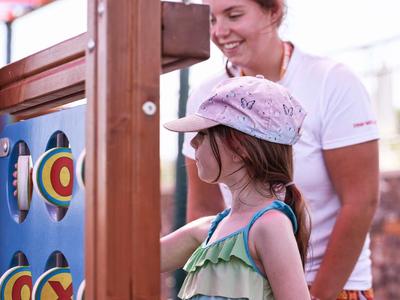 Bambina gioca a un gioco interattivo da parete sotto sorveglianza adulta all'aperto.