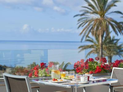 Terrasse mit gedecktem Frühstückstisch, Blick auf das Meer und Palmen im Hintergrund.