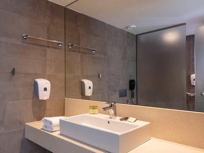 Bagno moderno in hotel con grande specchio, lavabo bianco, asciugamani e dispenser di sapone